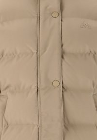 Beige puffer takki, jossa on tikattu muotoilu, napit ja sivutaskut. Joustava kangas, jossa on hienovarainen logo-ominaisuus rinnassa.