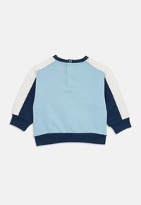 Sweatshirt bleu clair avec des manches raglan bleu marine et écru. Il dispose d'un col rond et d'une fermeture à trois boutons au dos.