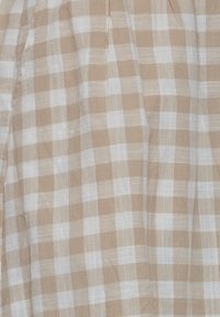 Vaalean beige ja valkoinen ruudullinen kangas, jossa on pehmeä, teksturoitu pinta ja hienovaraisia poimuja, esittäen neliöitä kudontamallissa.