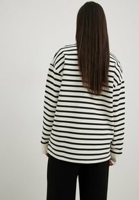 Maglietta a maniche lunghe a righe in bianco e nero, con vestibilità comoda, orlo arrotondato e polsini a coste. Il materiale sembra morbido e traspirante.