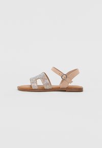 Sandales en cuir beige avec trois larges brides ornées de strass transparents, une bride à la cheville à boucle et une semelle plate en bois.