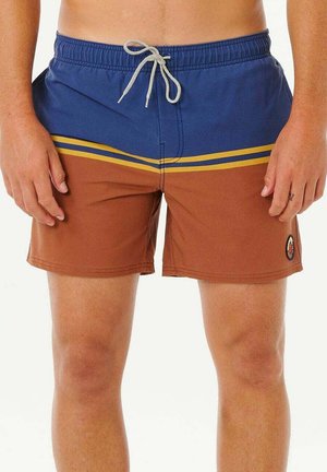 Mężczyzna w niebiesko-brązowych kąpielówkach z żółtymi paskami i białym ściągaczem, stojący z rękami swobodnie opuszczonymi wzdłuż ciała.