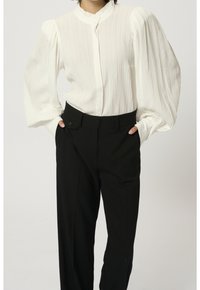 Witte, gestructureerde blouse met poffende mouwen en een Mandarin-kraag, gecombineerd met hoogwezige zwarte broek met knoopsluiting.
