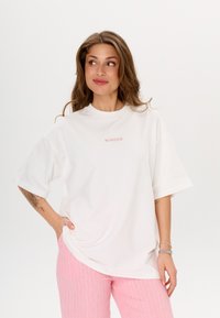 Witte oversized t-shirt met korte mouwen, voorzien van roze geborduurde tekst "MIRONS" op de borst. Zacht, glad katoen.