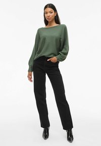 Grön ribbad långärmad topp i kombination med hög midja svarta jeans och svarta ankelstövlar, som ger en avslappnad silhuett och texturerad tyg.