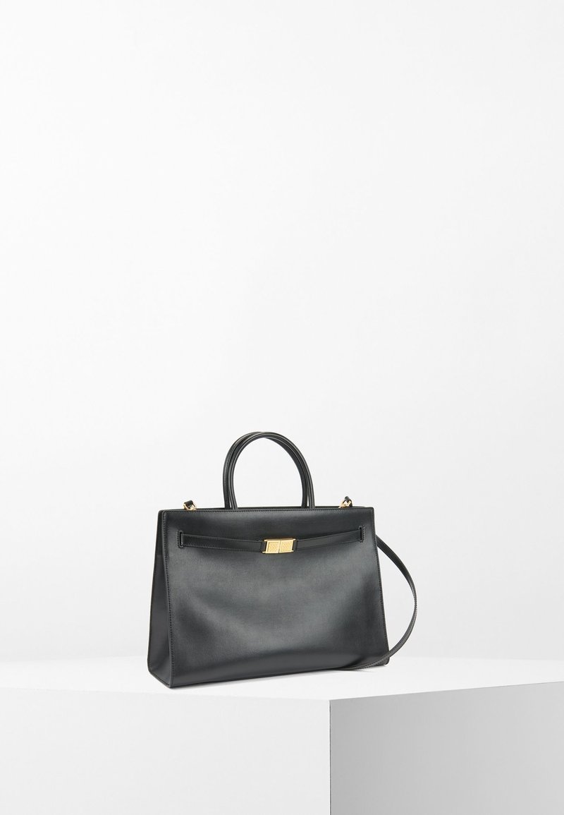 Svart läderhandväska med en strukturerad form, dubbla handtag, guldfärgad hårdvara och en framknäppning. Slät textur med en minimalistisk design.