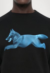 Svart hettegenser med et stort blått grafisk design av en hoppende ulv, laget med lineære mønstre for tekstur og visuell interesse.
