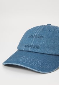 Denim baseball cap in dark blue with embroidered "SAMSØE" text. Features a curved peak and textured fabric. Classic adjustable strap at the back.