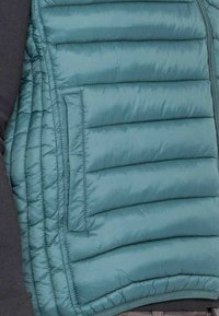 Gilet rembourré en teal avec des panneaux matelassés horizontaux, doté d'une poche latérale et d'une fermeture éclair à l'avant. Fabriqué en matériau léger et résistant à l'eau.