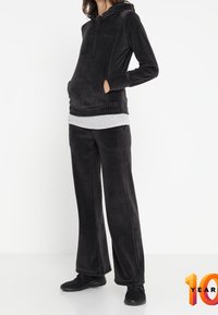 Sudadera de forro polar negra con un bolsillo frontal, camisa gris de capas y pantalones de forro polar negros a juego. Zapatillas deportivas negras completan el atuendo.