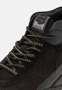 Černé tenisky z texturované kůže a semiše, černé a žlutě pruhované tkaničky a jazyková nášivka s potiskem dvou podávajících si rukou a textem "Filling Pieces".