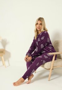 Violetit pyjamat, jotka on valmistettu pehmeästä kankaasta, sisältävät valkoisia sydänkuvioita. Yläosassa on pitkät hihat ja housut ovat tiukat.