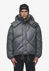 Grijs gewatteerd jack met een hoge kraag en oversized opvouwbare flappen. Voorzien van verstelbare trekkoorden en een logo op de borst.