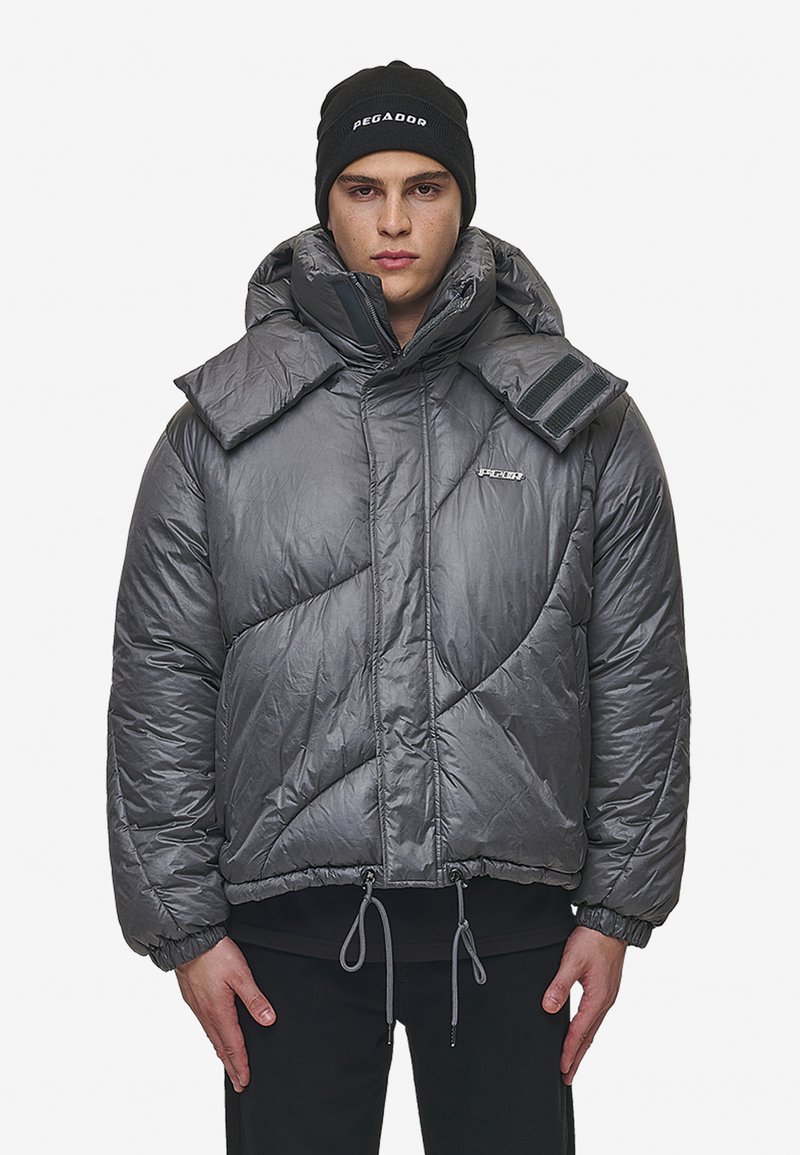 Grijs gewatteerd jack met een hoge kraag en oversized opvouwbare flappen. Voorzien van verstelbare trekkoorden en een logo op de borst.