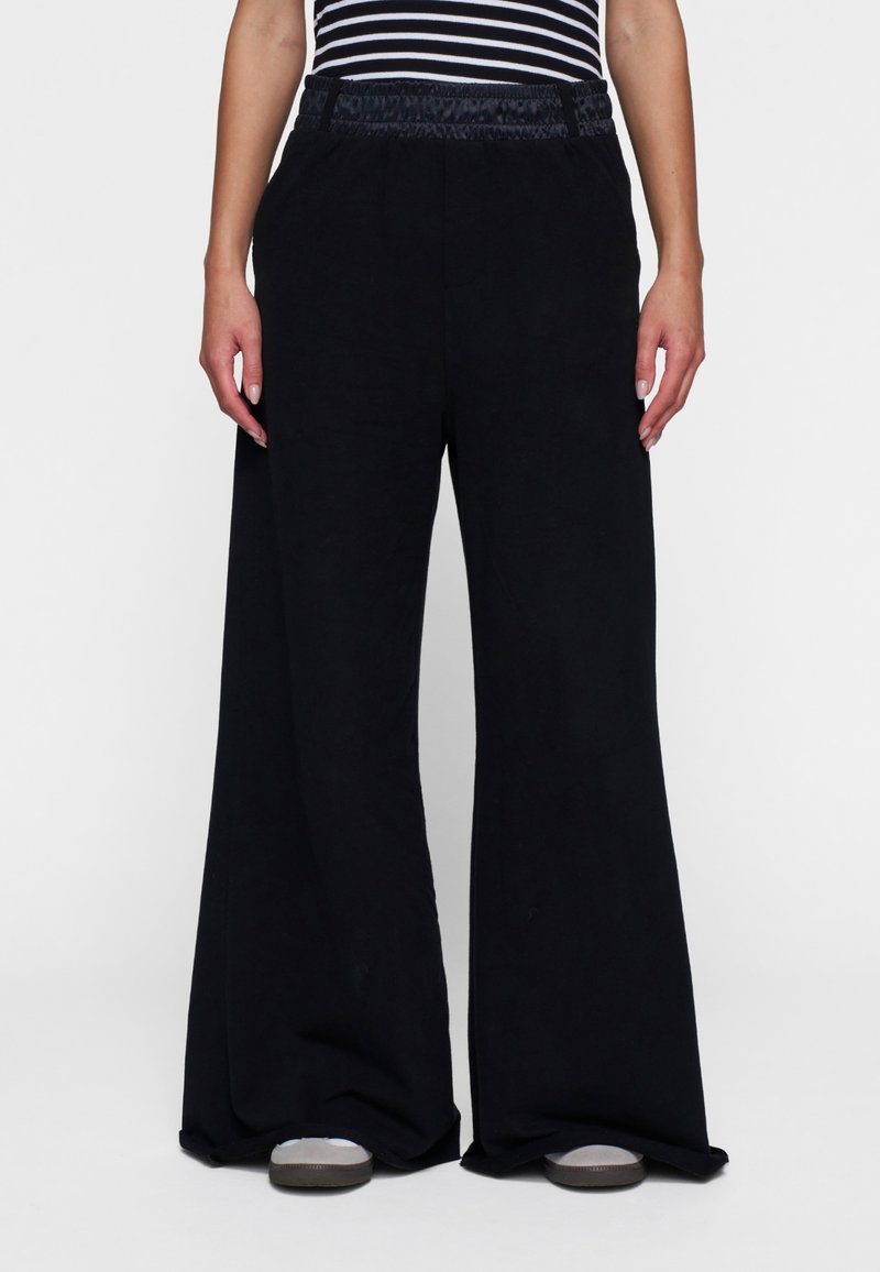 Zwarte wijde pantalon gemaakt van zachte stof, met een elastische tailleband. Soepele textuur met een losse, vloeiende uitstraling.
