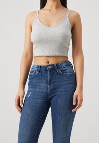 Grå ribbad crop top med tunna axelband, kombinerad med högmidjade blå denimjeans med lätt slitningar. En enkel och avslappnad design.