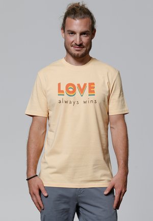 Helles gelbes Baumwoll-T-Shirt mit dem Text "LOVE" in Orange und Blau, darunter "always wins" in Braun. Kurze Ärmel, Rundhalsausschnitt.