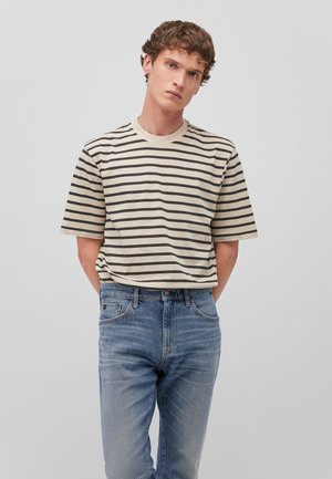 Beige striped t-shirt with dark stripes, short sleeves, and a crew neckline, paired with light blue denim jeans featuring front pockets.