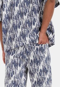 Korte mouwen overhemd en losse broek van een gestructureerde stof met een blauw-wit abstract patroon. Casual pasvorm met zijzakken.
