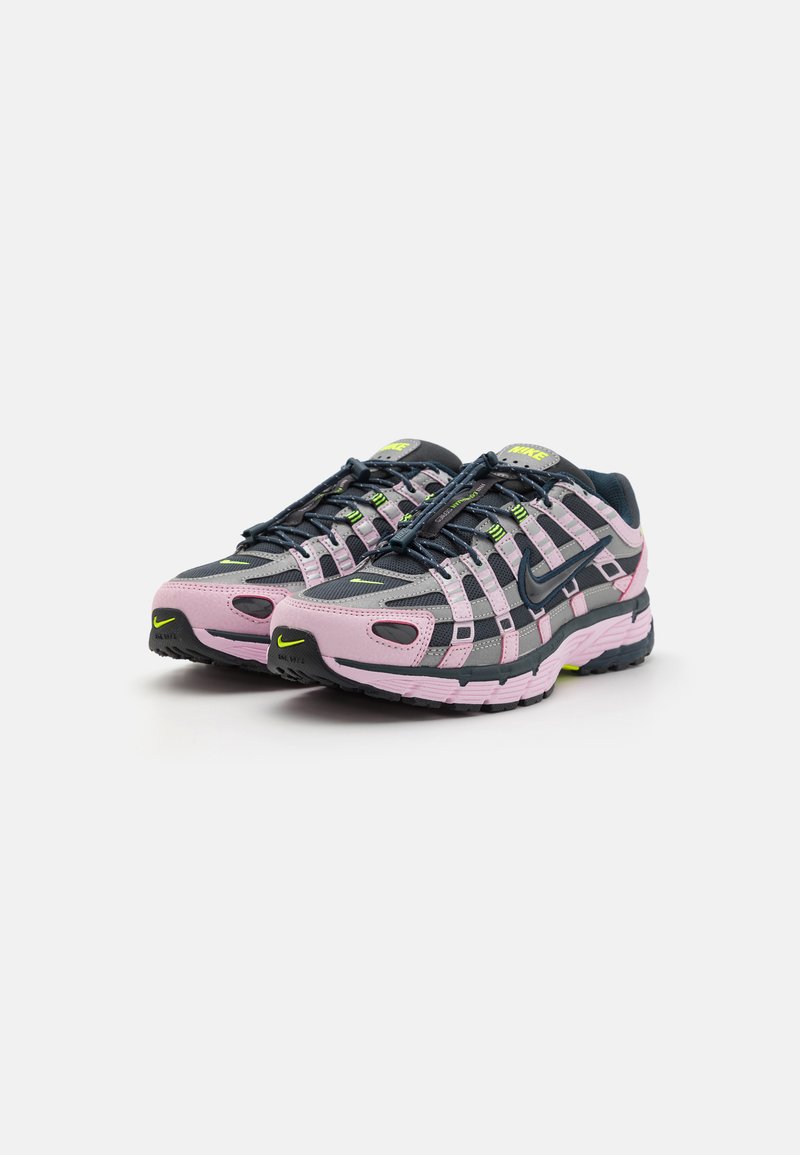 Nike sneakers met een roze en grijze mesh bovenwerk, zwarte accenten, felgele details en een gestructureerde rubberen zool.