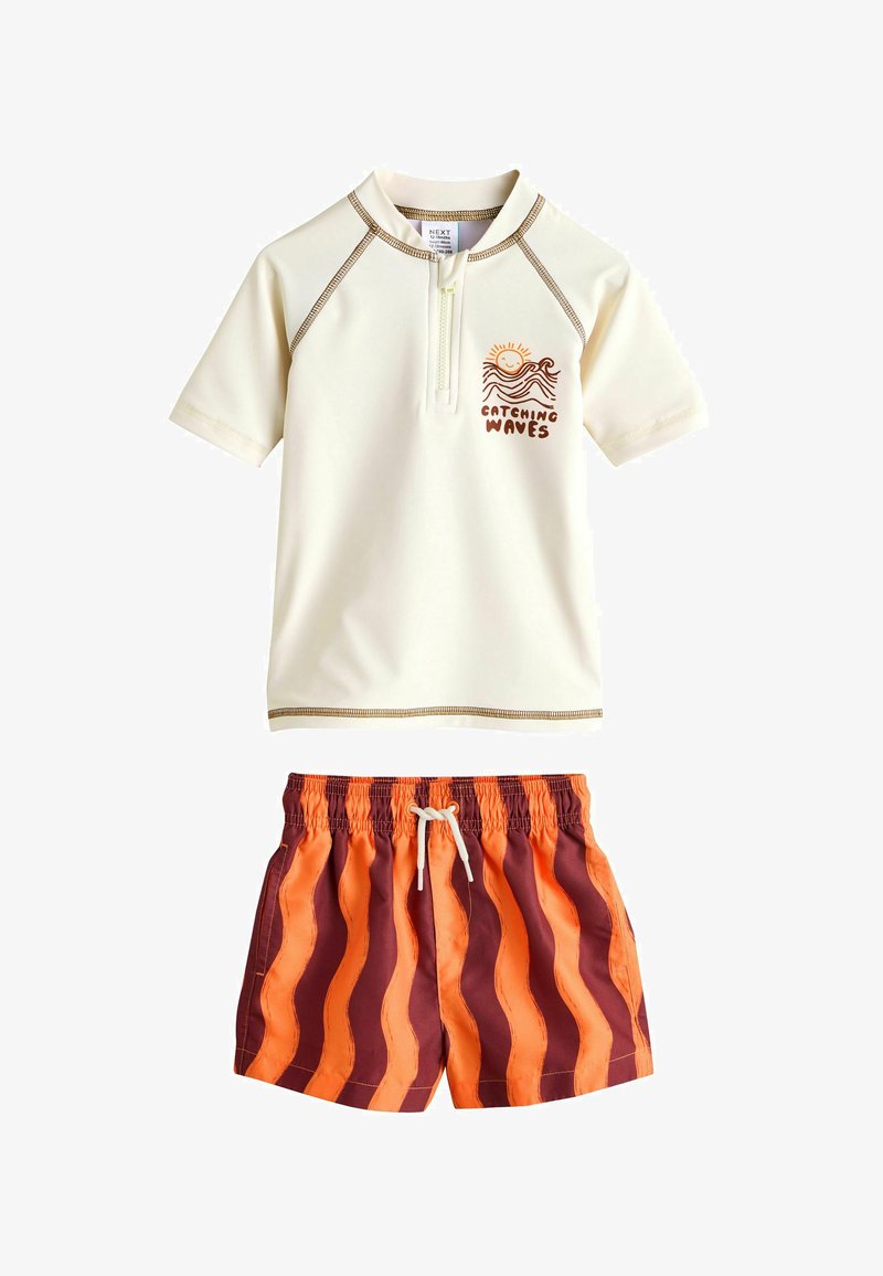T-shirt anti-UV crème à manches courtes avec un graphique de soleil et de vagues et le texte "Attraper les vagues", associé à un short de bain rayé ondulé orange et marron.