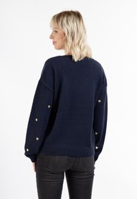 Marineblauer Strickpullover mit geripptem Saum und übergroßer Passform, mit kleinen goldenen Herzakzenten an den Ärmeln. Weiche Textur.