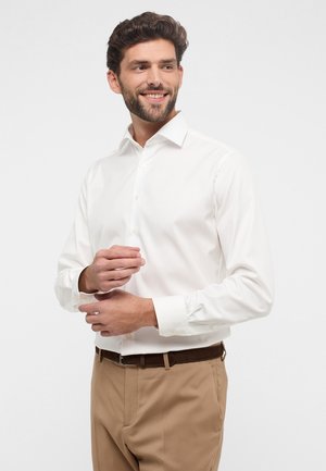 Witte overhemd met een klassieke kraag, knopen aan de voorkant en lange mouwen, gecombineerd met beige broek en een bruine riem.