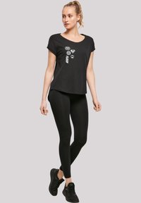 Svart T-skjorte med korte ermer og vid hals, med hvite grafiske trykk. Kombinert med svarte tights og svarte treningssko.