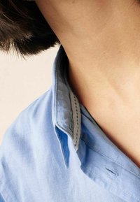 Chemise bleu clair à col avec une texture douce. Le col présente une couche intérieure contrastante et des détails de couture subtils.