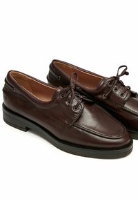 Paire de chaussures habillées en cuir marron foncé à lacets, bouts arrondis et semelles noires sur fond blanc.
