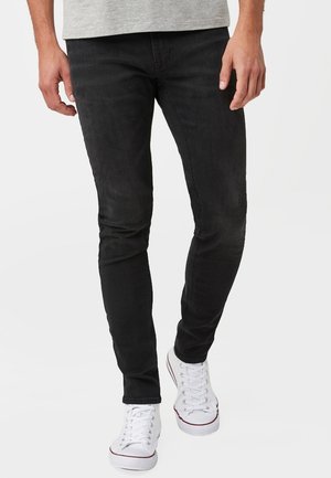 Vaqueros de denim ajustados negros con una textura desgastada, trabillas para cinturón y diseño de cinco bolsillos, combinados con zapatillas bajas blancas.