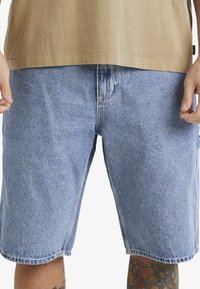 Vaaleansiniset denimit röyhkeällä leikkuulla, joissa on vyötärö, vyölenkit ja ommellut yksityiskohdat. Sileä pinta, polvipituinen.