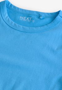 Svetlo modra majica z dolgimi rokavi in okroglo vratno odprtino, narejena iz gladke tkanine, na ovratniku ima etiketo z znamko "NEXT" in velikostjo "S".
