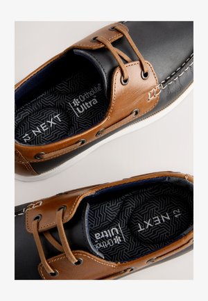 Pruun nahast pealmine osa tumesiniste detailidega, valge kummist tallaga ja dekoratiivse õmblusega. Varustatud Ortholite® Ultra sisetaldadega mugavuse tagamiseks.