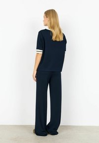 Temno modra majica s kratkimi rokavi s kremnimi črtastimi manšetami, kombinirana z ujemajočimi širokimi hlačami; mehka tkanina in sproščen kroj.