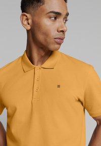 Geel poloshirt met een klassieke kraag, een drie-knopssluiting, gestructureerde stof en een klein logo op de borst.