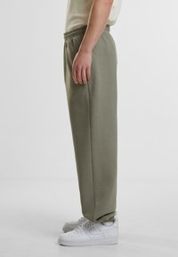 Lys olivengrønne joggebukser med elastisk midje og avsmalnende mansjetter, kombinert med hvite sneakers. Glatt stoffstruktur, avslappet passform.