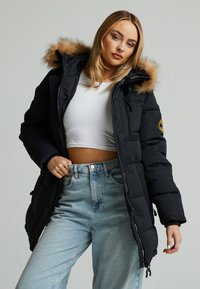 Crni podstavljeni parkas s kapuljačom obloženom krznom, s zatvaranjem na zip, podesivim uzicama i oznakom na rukavu.