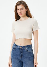 Crème-kleurige cropped t-shirt met een geribbelde textuur en korte mouwen, gecombineerd met high-waisted blauwe denim jeans met een knoopsluiting.