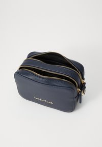 Trousse de toilette en cuir marine avec des fermetures éclair dorées, deux compartiments et un logo doré. Texture lisse et forme rectangulaire.