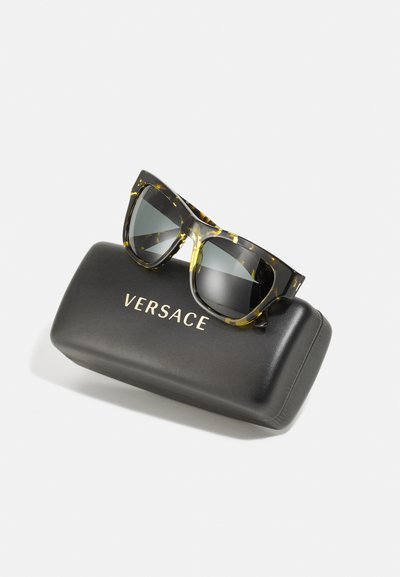 Ochelari de soare Versace cu rame din cheratină țestoasă neagră și galbenă și lentile întunecate, așezați pe un etui rigid negru cu litere aurii.