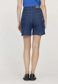 Shorts en denim bleu foncé avec une taille mi-haute, ourlet roulé et deux poches arrière. Présente une étiquette de marque en cuir marron sur la taille.