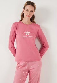 Blusa de manga larga rosa con un gráfico de estrella blanca y el texto "Siempre me encanta el invierno"; combinada con pantalones rosas adornados con pequeñas estrellas blancas.