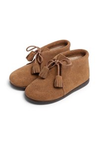 Botas de tobillo de ante marrón con punta redonda, cordones con borlas y suela plana de goma, adornadas con detalles perforados en la parte delantera.
