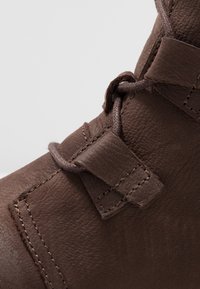 Lähikuva ruskeasta nahkakengästä, jossa on teksturoitu pinta, nauha kulkee ommeltujen silmukoiden läpi pehmustetussa yläosassa.