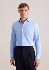 Camicia azzurro chiaro a maniche lunghe con colletto button-down e una texture liscia, abbinata a pantaloni scuri a pieghe.