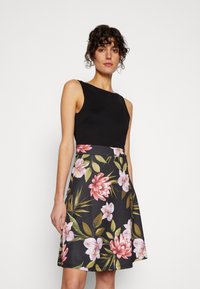 Sleeveless black dress with a floral print in pink and green on a dark background, featuring a fitted bodice and flared skirt.