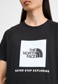 Camiseta negra de The North Face con un logo y texto en blanco "NEVER STOP EXPLORING" en el frente. Mangas cortas, cuello redondo.