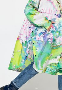 Barevný dlouhý kabát s kombinací zelených, růžových a modrých abstraktních vzorů, vyrobený z lehkého materiálu se zapínáním na patentky.