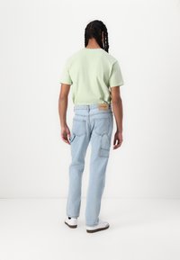 Lichtgroene katoenen t-shirt met korte mouwen, gecombineerd met lichtblauwe denim broek met opgestikte zakken en een tan label bij de tailleband.